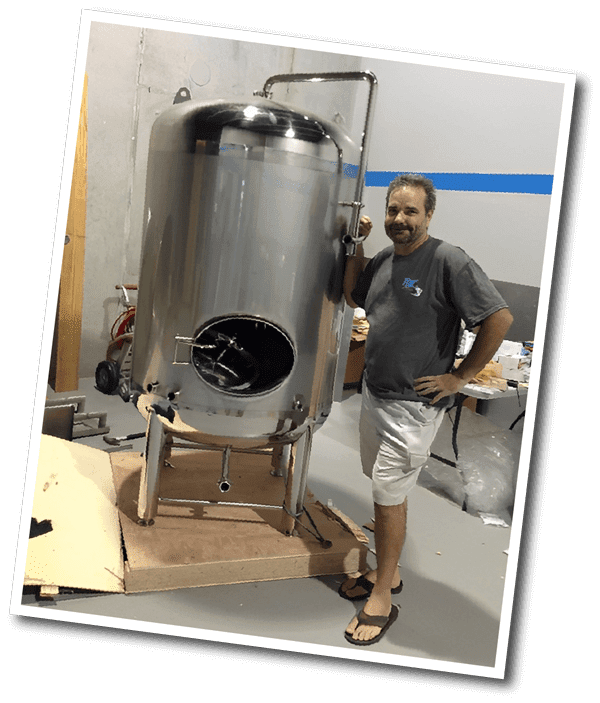 A man standing next to a stainless steel tank.